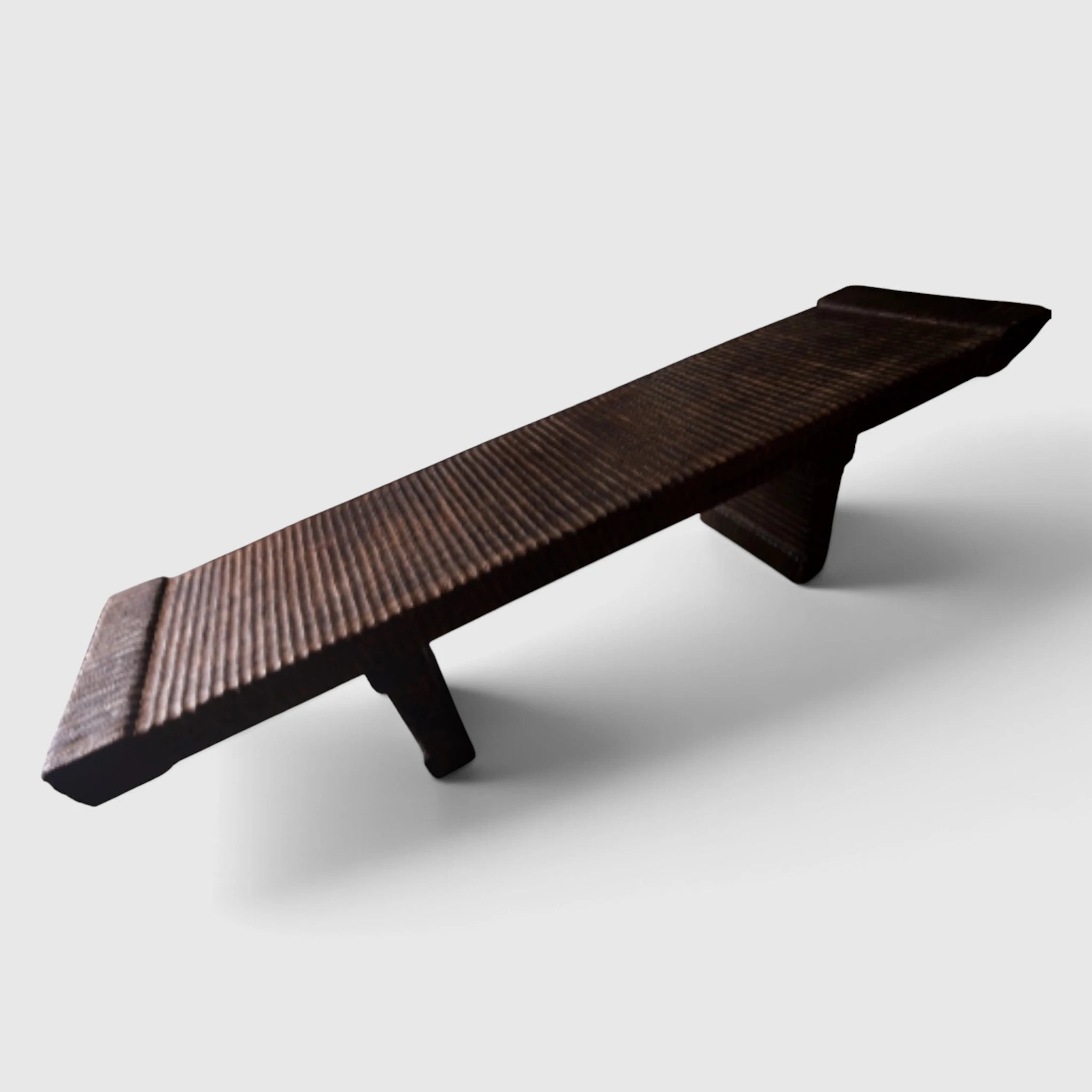 Angled studio shot of the Senja hand-carved solid mango wood bench showing its long profile, sculpted legs, and dark charred espresso finish.