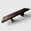 Angled studio shot of the Senja hand-carved solid mango wood bench showing its long profile, sculpted legs, and dark charred espresso finish.