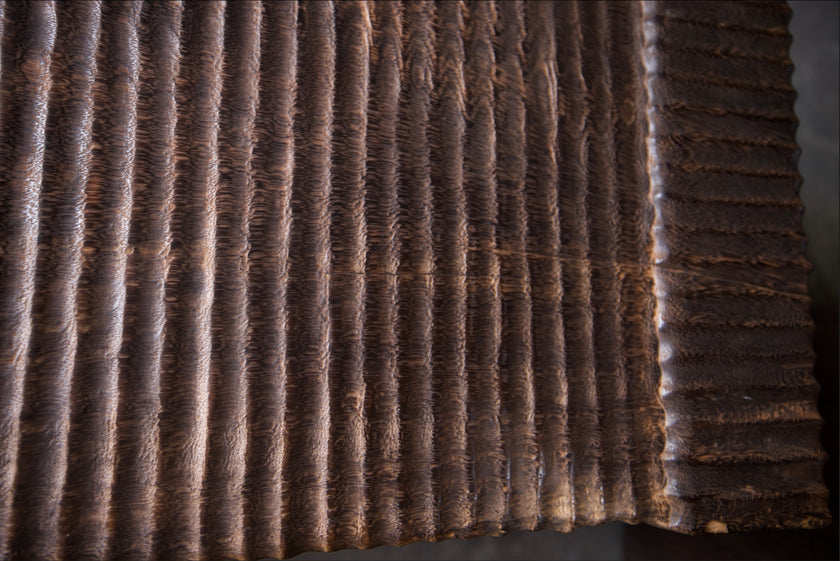 Extreme macro detail shot showing the hand-carved ridged textures and traditional fire-torched espresso finish on the solid mango wood bench.