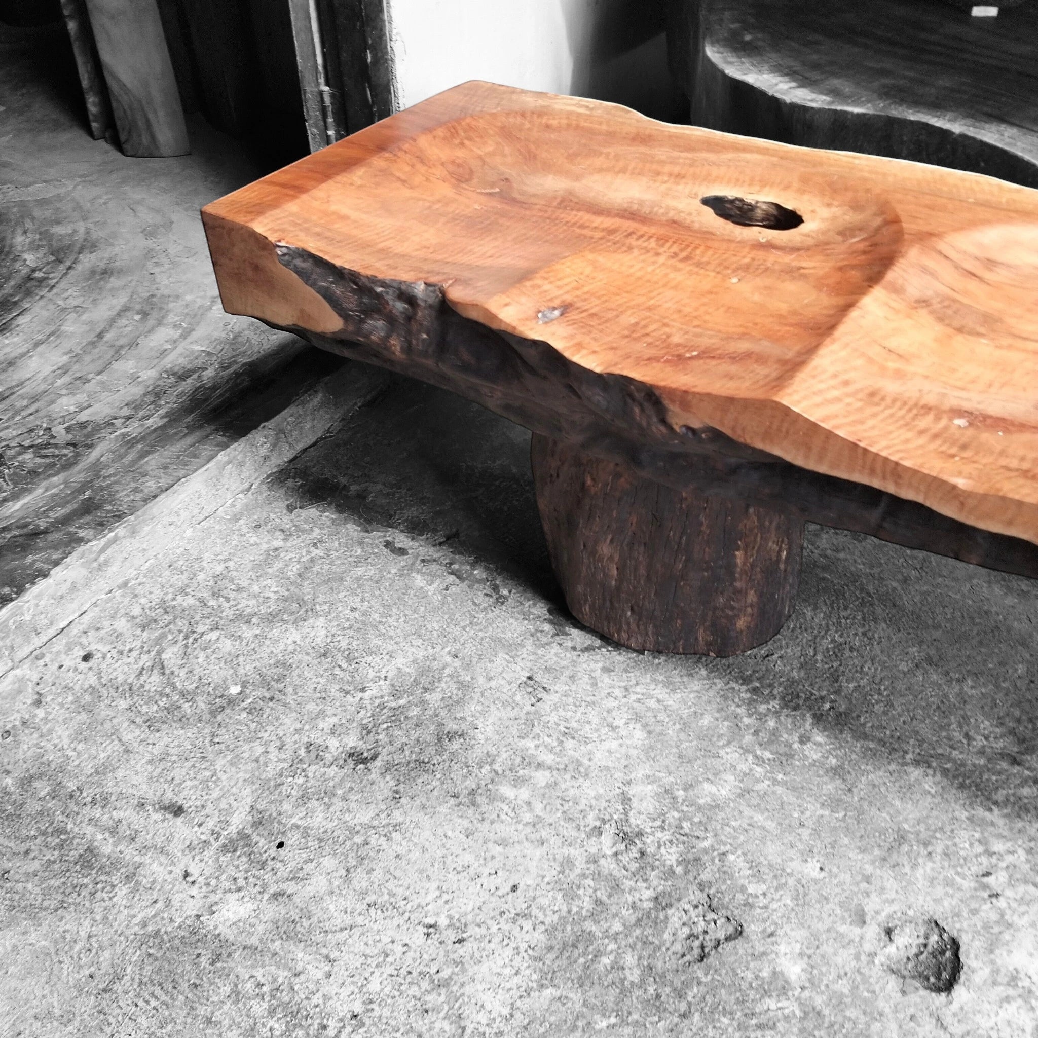 Bespoke Senja modern organic bench in carved lychee wood styled on an industrial raw concrete floor to showcase luxury architectural texture contrast.