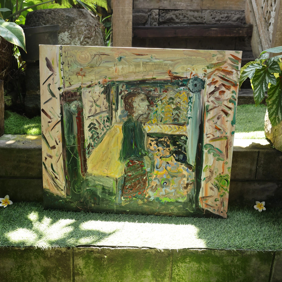 Berkaca (2026), a one-of-a-kind acrylic painting on canvas by emerging Balinese artist I Wayan Dendy Permana Putra — displayed outside his family art gallery on a grass-covered stone ledge amid tropical foliage, with a carved stone feature by the artist's father, established artist I Nyoman Bratayasa, visible behind it — photographed and curated by Senja Living.