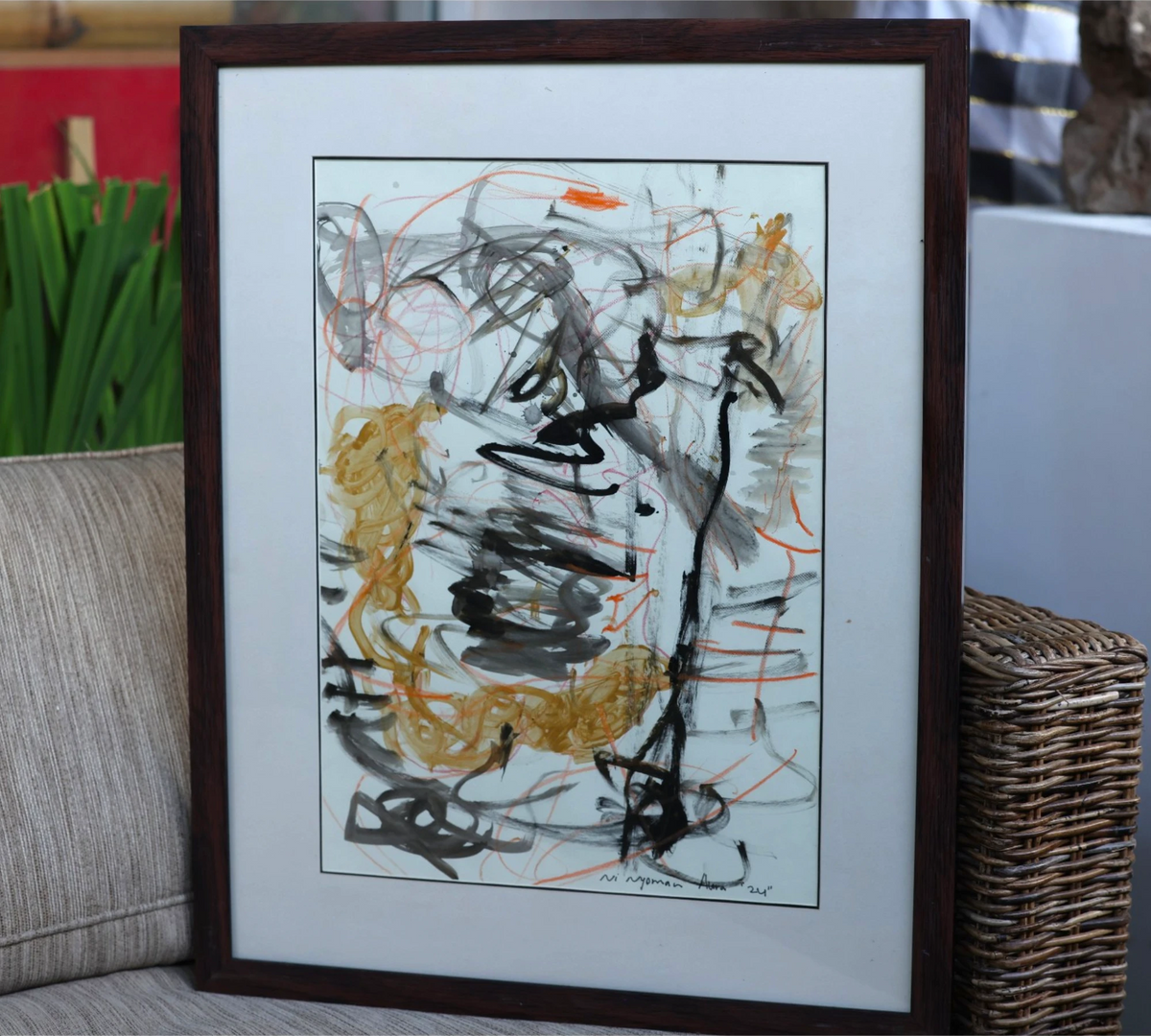 Naga (2024), a one-of-a-kind acrylic painting on paper by talented young emerging Balinese artist Ni Nyoman Aura Komala Dewi, displayed in its dark wood frame and white mat on a wicker chair directly outside her family’s art gallery in Lodtunduh village, Bali, beside the gallery’s glass wall and doors — photographed and curated by Senja Living.