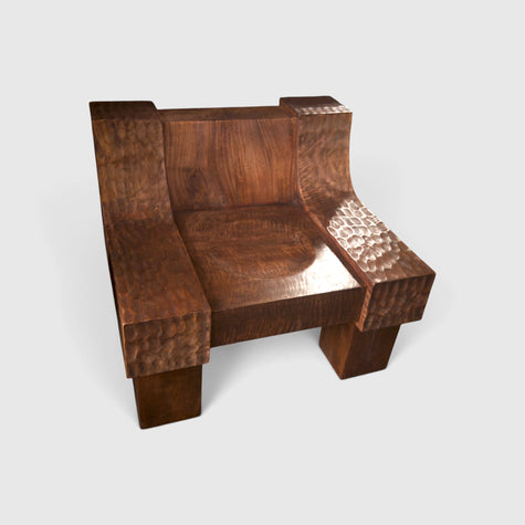 Hero shot of the modern organic brutalist sculptural lounge chair No.99, in solid mango wood with fire-torched charred warm chestnut tones and hand-chiseled textured armrests by Senja Living.