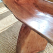 Solid lychee wood bench close-up highlighting the smooth polished finish meeting the incredible precipice of the natural live edge over a woven coastal seagrass rug.