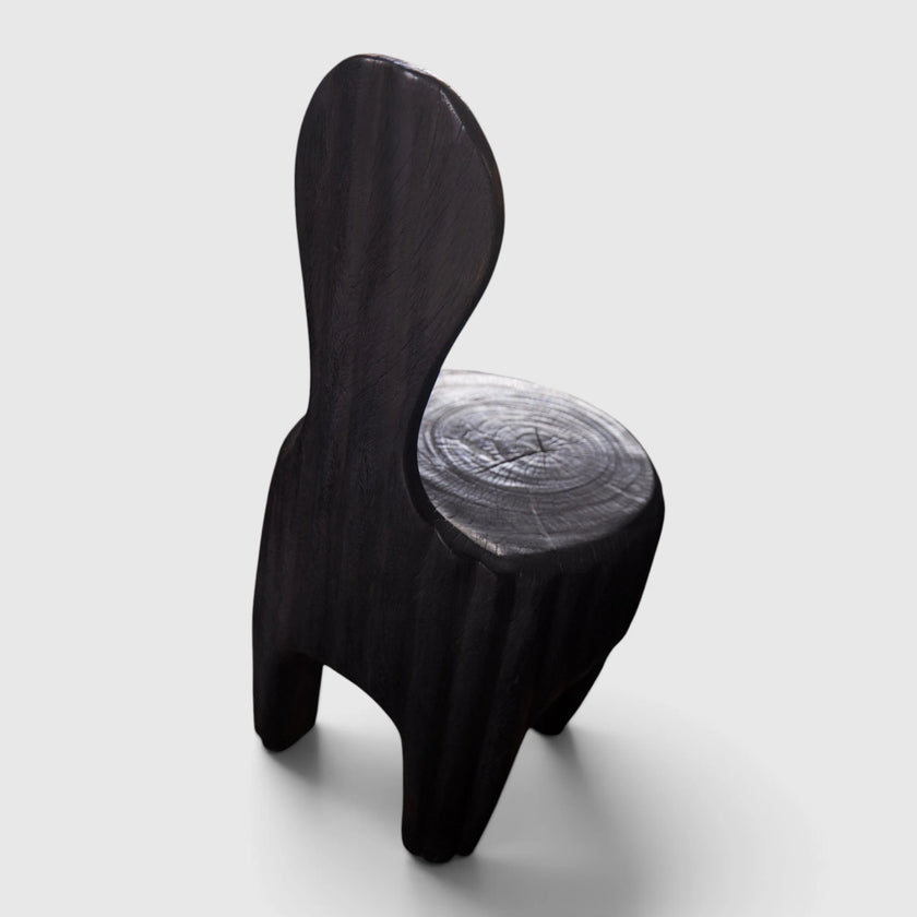 The Senja Living Bespoke Spoon-Back Chair is fire-torched from a single block of solid mango wood featuring a tall spoon-shaped backrest and a polished seat showing natural wood grain rings.