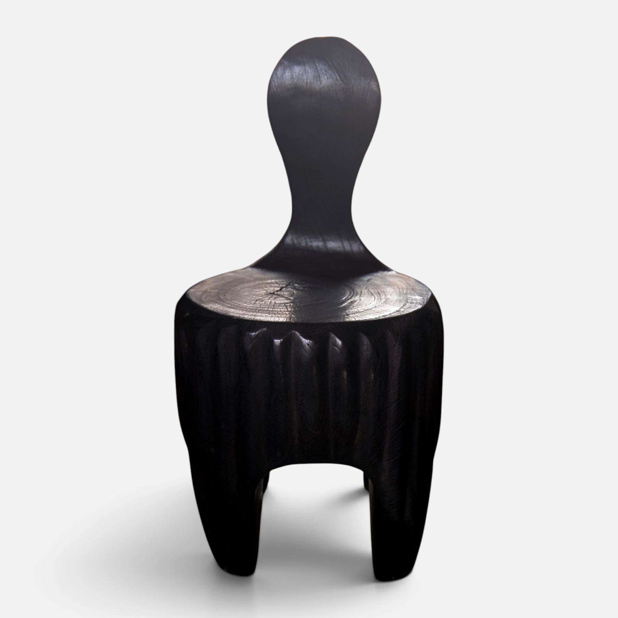 The Senja Living Bespoke Spoon-Back Chair is hand-sculpted from a single block of solid mango wood featuring an elegant fire-torched charred charcoal black finish.